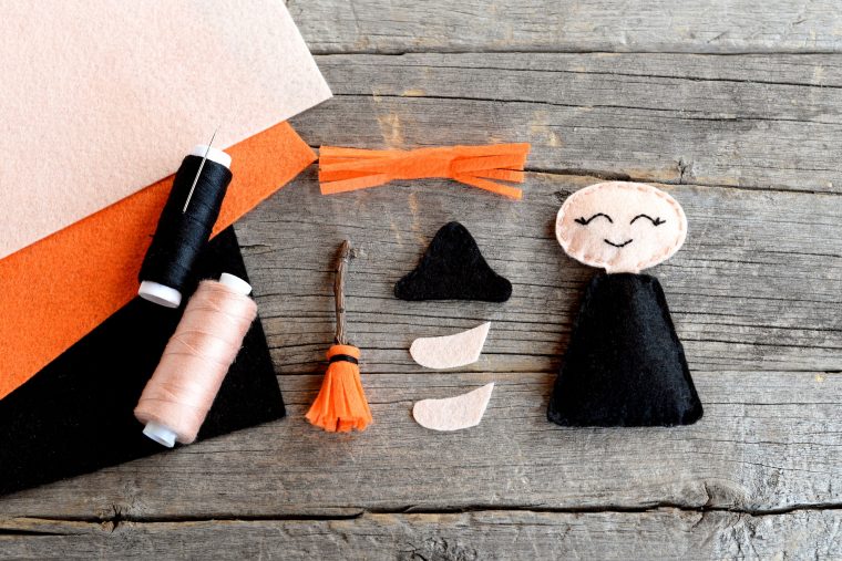how to sew a halloween witch doll. step. halloween witch ornament details, scissors, thread, needle, felt sheets set on wooden background. handmade crafts for children and beginners. top view
