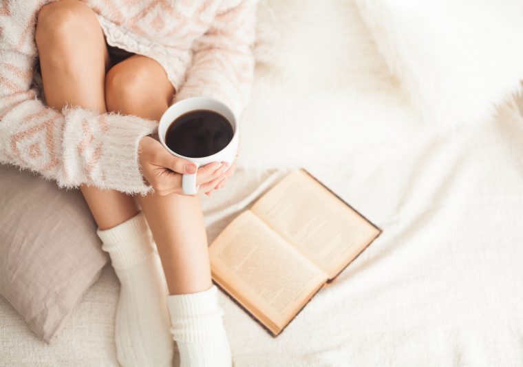 woman on the bed with old book and cup of coffee in hands